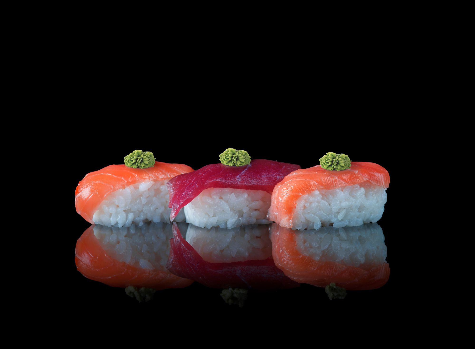 Três peças de nigiri sob luz pontual, em fundo obsidiana
